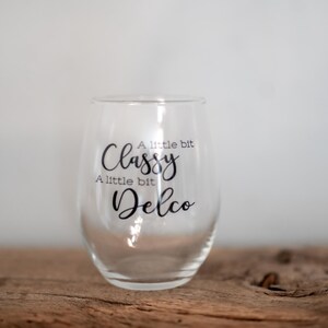 Puede incluir: Una copa de vino de vidrio transparente con el texto "A little bit Classy A little bit Delco" impreso en el lateral.