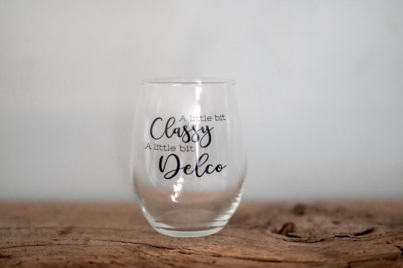 Puede incluir: Una copa de vino de vidrio transparente con el texto "A little bit Classy A little bit Delco" impreso en el lateral.