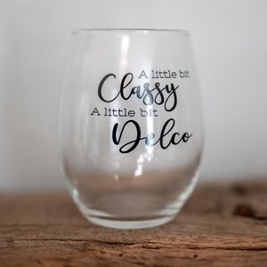Puede incluir: Una copa de vino de vidrio transparente con el texto "A little bit Classy, A little bit Delco" impreso en el lateral.