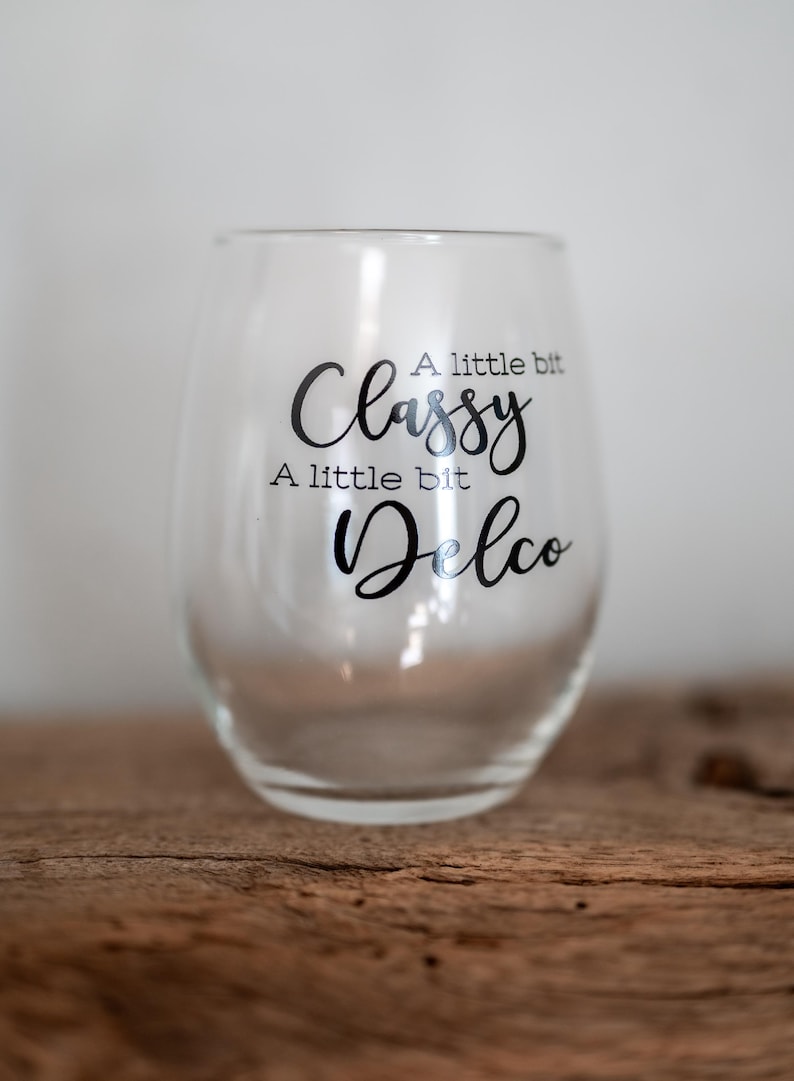 Puede incluir: Una copa de vino de vidrio transparente con el texto "A little bit Classy, A little bit Delco" impreso en el lateral.