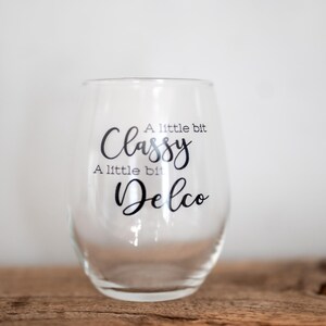 Puede incluir: Una copa de vino de vidrio transparente con una calcoman&iacute;a de vinilo negro que dice "A little bit Classy, A little bit Delco".