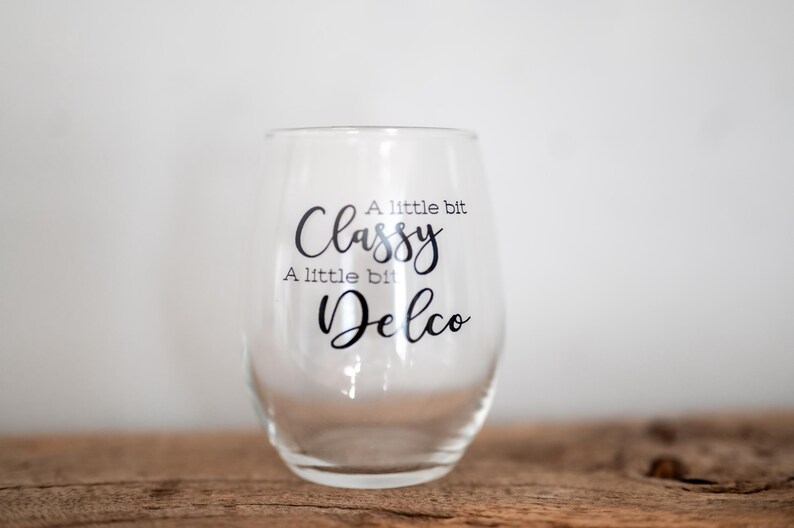 Puede incluir: Una copa de vino de vidrio transparente con una calcoman&iacute;a de vinilo negro que dice "A little bit Classy, A little bit Delco".