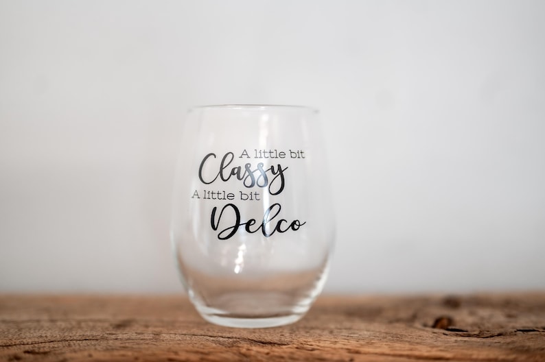 Puede incluir: Una copa de vino de vidrio transparente con el texto "A little bit Classy A little bit Delco" impreso en el lateral.
