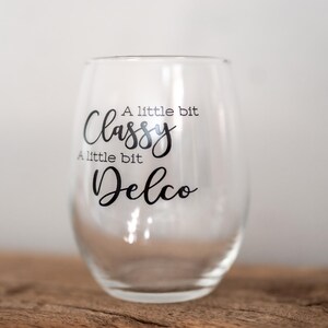 Puede incluir: Una copa de vino de vidrio transparente con el texto "A little bit Classy, A little bit Delco" impreso en el lateral.