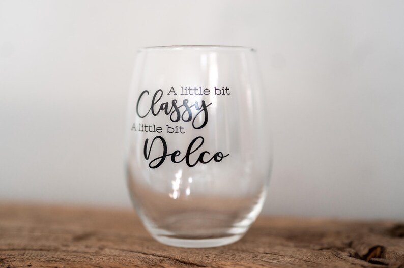 Puede incluir: Una copa de vino de vidrio transparente con el texto "A little bit Classy, A little bit Delco" impreso en el lateral.