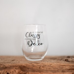 Puede incluir: Una copa de vino de vidrio transparente con el texto "A little bit Classy, A little bit Delco" impreso en el lateral.