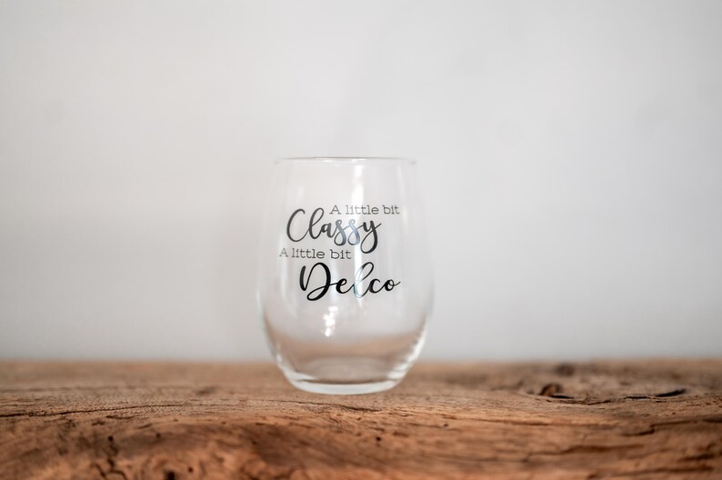 Puede incluir: Una copa de vino de vidrio transparente con el texto "A little bit Classy, A little bit Delco" impreso en el lateral.