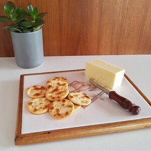 May include: A wooden serving board with a floral design and a block of cheese, a butter knife, and crackers on top.