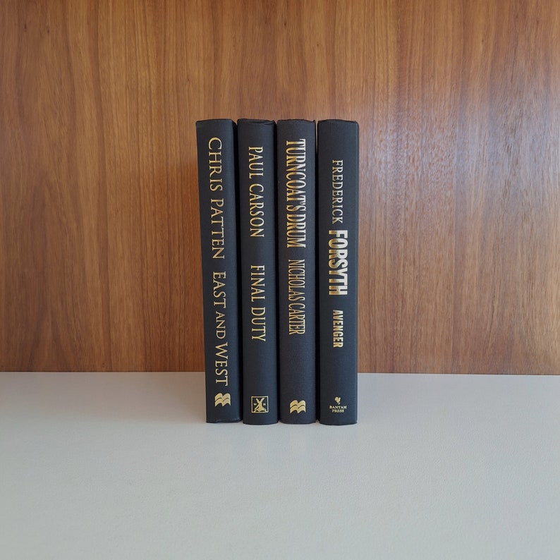 Puede incluir: Un conjunto de cuatro libros de tapa dura negros con letras doradas en el lomo. Los t&iacute;tulos son "East and West" de Chris Patten, "Final Duty" de Paul Carson, "Turncoat's Drum" de Nicholas Carter y "Avenger" de Frederick Forsyth.