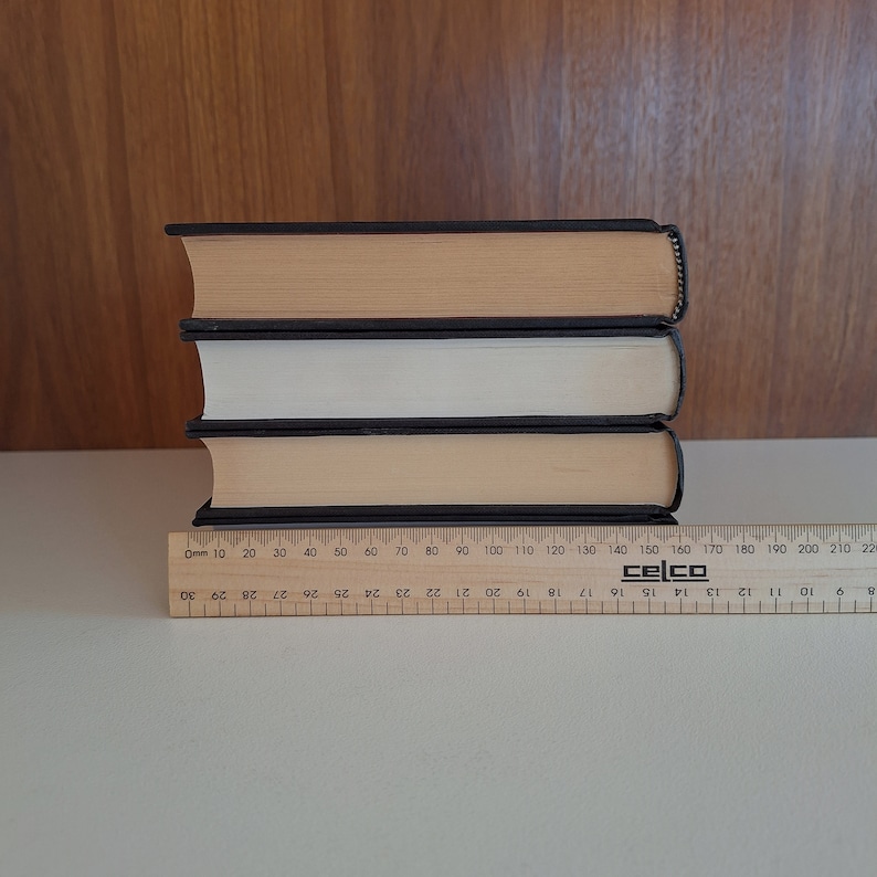 Puede incluir: Tres libros de tapa dura apilados uno encima del otro. El libro de arriba es marr&oacute;n con una encuadernaci&oacute;n negra, el libro del medio es blanco con una encuadernaci&oacute;n negra y el libro de abajo es beige con una encuadernaci&oacute;n negra.
