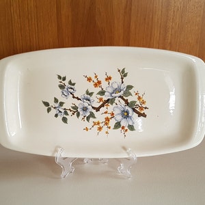 May include: White rectangular ceramic serving dish with a floral design. The design features blue and white flowers with green leaves and yellow stems.