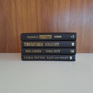 Puede incluir: Una pila de cuatro libros de tapa dura negros con letras doradas en los lomos. Los t&iacute;tulos son "Avenger" de Frederick Forsyth, "Turncoat's Drum" de Nicholas Carter, "Final Duty" de Paul Carson y "East and West" de Chris Patten.