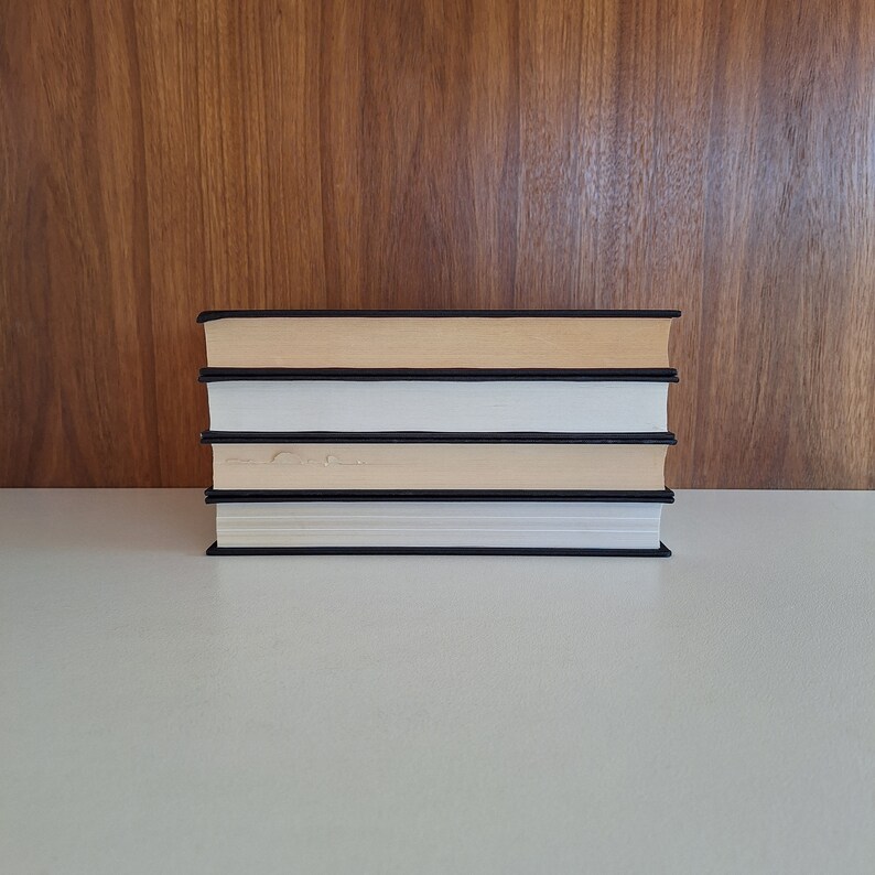 Puede incluir: Una pila de cuatro libros con cubiertas negras y p&aacute;ginas blancas. Los libros est&aacute;n dispuestos en una pila vertical sobre una superficie blanca.