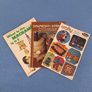 May include: Three vintage craft books on a blue surface. Titles include "What in the Macrame is it?", "Symphony of Strings", and "Crafty". The "Crafty" book features a panda bear and various craft ideas.