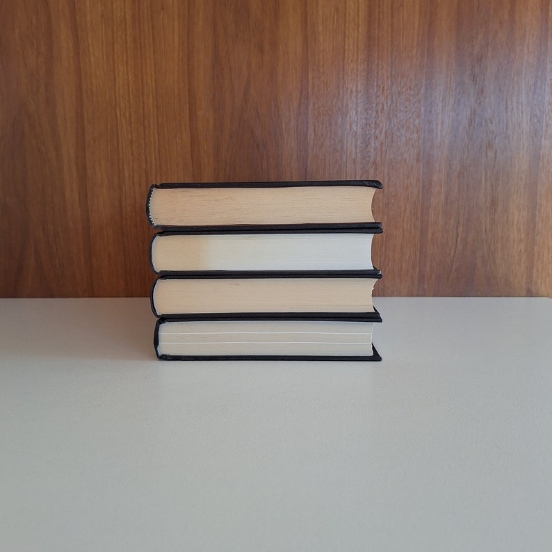 Puede incluir: Una pila de cuatro libros con cubiertas negras y p&aacute;ginas de color crema. Los libros est&aacute;n dispuestos en una pila ordenada sobre una superficie blanca.