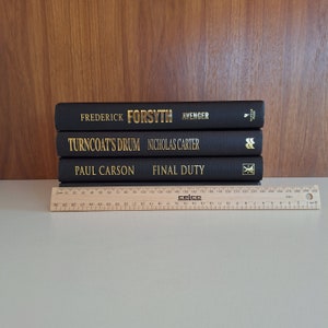 Puede incluir: Tres libros encuadernados en tapa dura de color negro apilados uno encima del otro. El libro de arriba es "Avenger" de Frederick Forsyth. El libro del medio es "Turncoat's Drum" de Nicholas Carter. El libro de abajo es "Final Duty" de Paul Carson.