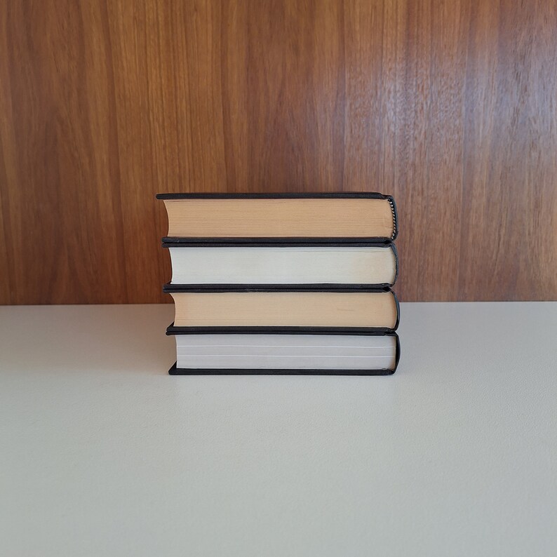 Puede incluir: Una pila de cuatro libros con cubiertas negras y p&aacute;ginas de color crema. Los libros est&aacute;n apilados sobre una superficie blanca.