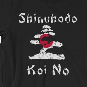 Pode incluir: T-shirt preto com texto branco e um gráfico de uma árvore e um círculo vermelho. O texto na camiseta diz "Shinuhodo Koi No". O design é desgastado, dando-lhe um visual vintage. A camiseta é feita de um material macio.