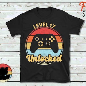May include: Black t-shirt with a retro-style graphic of a video game controller and the text "Level 17 Unlocked".