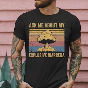 Puede incluir: Camiseta negra con un gráfico de estilo vintage de una nube de hongo en explosión. El texto "Ask me about my explosive diarrhea" está impreso debajo del gráfico.