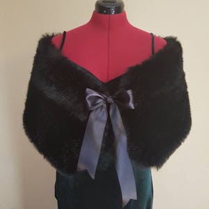 May include: A black faux fur shawl with a large satin bow. The shawl is draped over a dress form.
