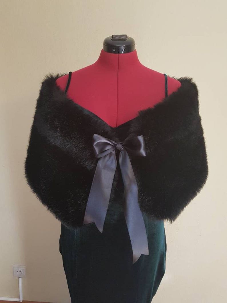 May include: A black faux fur shawl with a large satin bow. The shawl is draped over a dress form.
