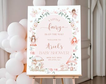 Può includere: Un cartello di benvenuto per baby shower su un cavalletto di legno. Il cartello è rosa con illustrazioni floreali e di fate e il testo "A Little Fairy is on the Way! Welcome to Ariel's Baby Shower". Palloncini bianchi e oro rosa sullo sfondo.