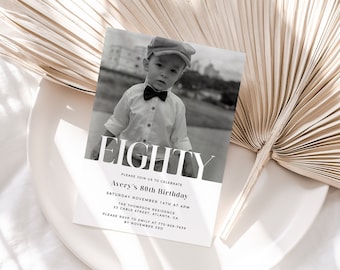 Op de afbeelding: Een zwart-witte verjaardagsuitnodiging met het woord "EIGHTY" in vetgedrukte, witte letters. De uitnodiging is voor Avery's 80e verjaardag en bevat de datum, tijd en locatie van het evenement. Een zwart-witte foto van een jonge jongen met een strikje en een pet is op de achtergrond.