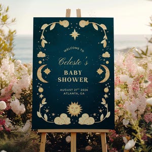 May include: A navy blue baby shower sign on a wooden easel, featuring gold celestial designs. The sign reads "Welcome to Celeste's Baby Shower" with the date August 21st, 2026, and location Atlanta, GA.