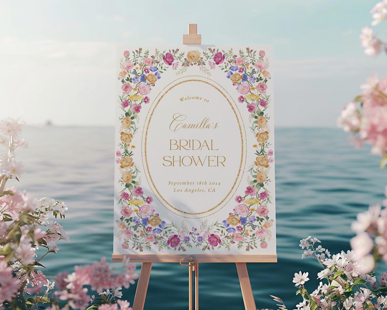 Puede incluir: Un cartel blanco con un borde floral y letras doradas anunciando una despedida de soltera para Camilla. El texto dice "Bienvenida a la despedida de soltera de Camilla el 18 de septiembre de 2023 en Los &Aacute;ngeles, California."