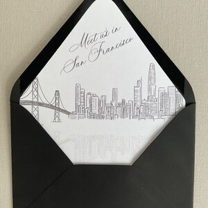 May include: A white envelope with a black border and a black and white illustration of the San Francisco skyline, including the Golden Gate Bridge. The text "Meet us in San Francisco" is written in cursive on the envelope.