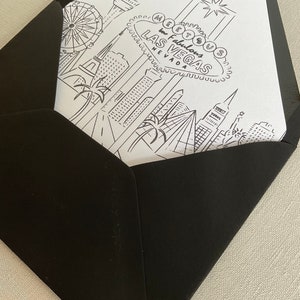 May include: A black and white illustration of the Las Vegas skyline, including the iconic "Welcome to Fabulous Las Vegas" sign, a Ferris wheel, and palm trees. The illustration is printed on a white card inside a black envelope.