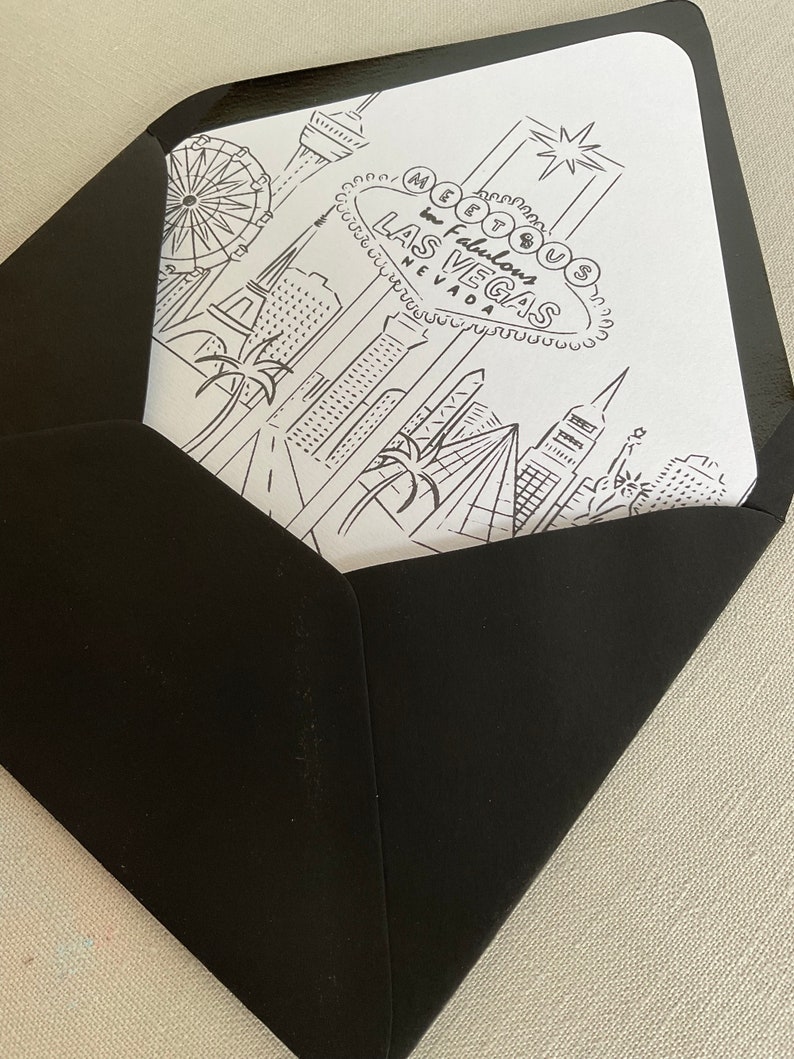 May include: A black and white illustration of the Las Vegas skyline, including the iconic "Welcome to Fabulous Las Vegas" sign, a Ferris wheel, and palm trees. The illustration is printed on a white card inside a black envelope.