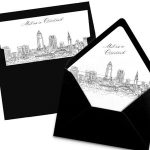 May include: Two black envelopes with a white card inside. The card features a black and white line drawing of a city skyline and the text "Meet us in Cleveland" in cursive. The envelopes are open, revealing the card's design.