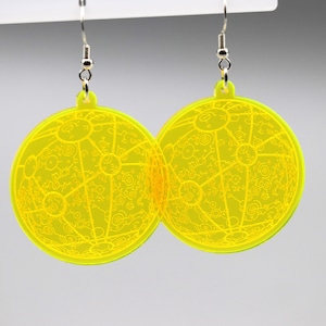 May include: A pair of yellow circular earrings with a detailed etched design. The earrings are made of acrylic and have silver hooks.