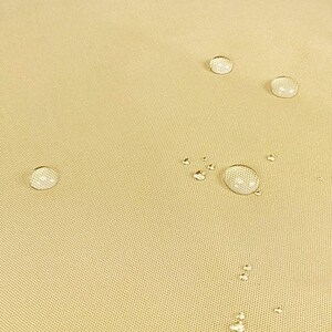May include: Close-up of a beige fabric surface with several water droplets on it. The fabric has a subtle texture and appears to be water-resistant.