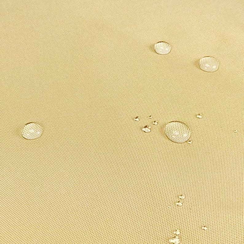May include: Close-up of a beige fabric surface with several water droplets on it. The fabric has a subtle texture and appears to be water-resistant.