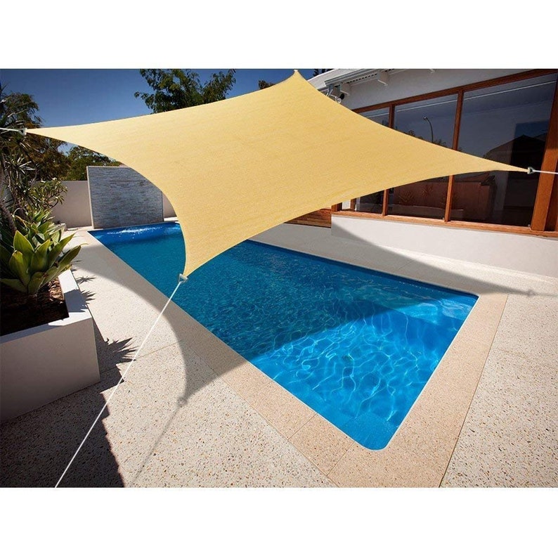 May include: A beige rectangular shade sail provides shade over a blue swimming pool. The sail is attached to poles and is secured with ropes.