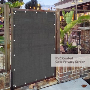 May include: A dark gray PVC coated gate privacy screen with white grommets. The screen is attached to a metal gate with a brick wall behind it.