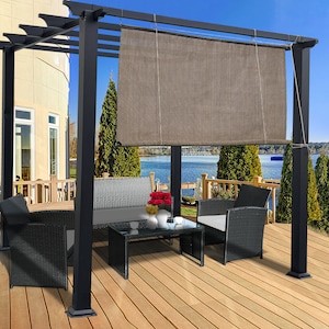 May include: A black pergola with a brown shade, a glass-top coffee table, and black wicker furniture. The outdoor setting includes a wooden deck, a lake, and a house in the background. The scene is set on a sunny day.