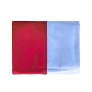 May include: A rectangular flag with a vertical split design. The left side is a solid deep red, and the right side is a light blue with a subtle grid pattern. The two sections are sewn together with a red seam.