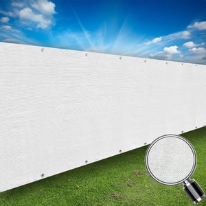 May include: White privacy fence made of woven mesh material. The fence is attached to a wooden post with metal grommets. The fence is shown against a green grassy lawn and a blue sky with white clouds.