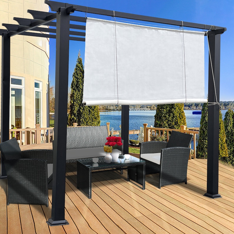May include: A black pergola with a white retractable shade, set on a wooden deck overlooking a lake. The outdoor furniture includes a sofa, two armchairs, and a glass-top coffee table. Red flowers and white vases add color.
