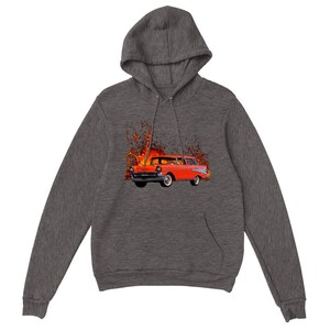Könnte beinhalten: Dunkelgrauer Kapuzenpullover mit einem auffälligen Grafikdesign. Es zeigt einen klassischen roten Kombi, der von Flammen umgeben ist. Das Auto hat Weißwandreifen und Chromdetails. Das Design befindet sich mittig auf der Vorderseite des Sweatshirts.