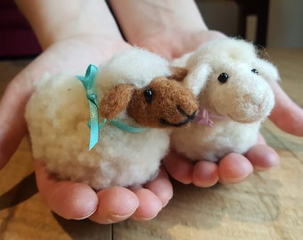 May include: Two small, white, fluffy sheep made of felt. One sheep has a brown face and a turquoise bow. The other sheep has a pink bow.