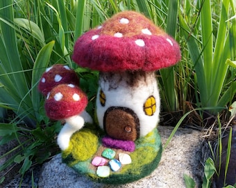 May include: A whimsical felt mushroom house with a red and white mushroom cap, a white body with a brown door and yellow windows, and a green base with colorful stones.