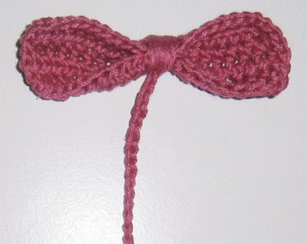 May include: A pink crocheted bow with a long tail. The bow is made of yarn and has a delicate, feminine look.
