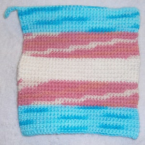 May include: Hand-knitted square featuring the transgender pride flag colors: light blue, pink, and white. The flag design is created with horizontal stripes. The top corner has a small loop. The item is made of a textured yarn.