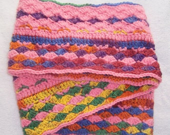 May include: A colorful crocheted scarf with a pink, red, blue, green, and yellow pattern. The scarf is folded in half and has a textured, woven design.