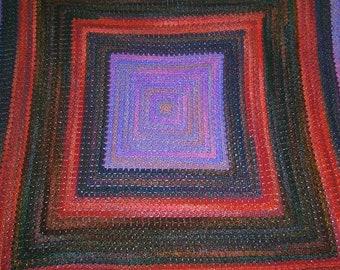May include: A square crocheted blanket with a multi-colored design. The blanket features a series of concentric squares in shades of red, purple, and brown.